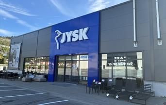 Fasaden til JYSK Lyngdal i Handelsparken, med blå logo og utemøbler utstilt foran inngangen.