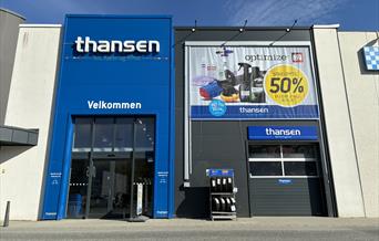 Inngangen til thansen Lyngdal i Handelsparken, med blå fasade og reklamebanner.