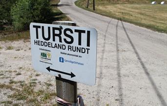 Bilde av skilt "Tursti, Heddeland rundt. Initiativtakere: NBK norges bygdekvinnelag. Øyslebø bygdekvinnelag. Støttet økonomisk av: GjensidigeStiftelsen."