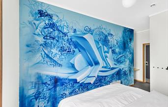 hotellvegg med streetart i blått med signaturer og noe som ser ut som 3D og virker som om det står ut fra veggen.