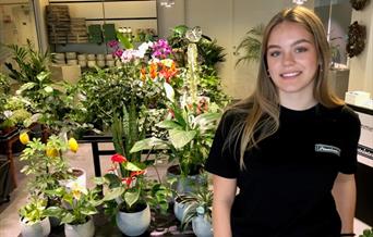 Smilende jente i svart t-skjorte foran blomster og planter.