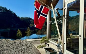 Fasade Øygarden Gård, med flagg i flaggstanga og utsikt ut til vannet