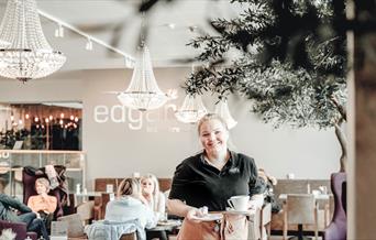 Smilende kvinne i Edgars uniform med kaffe i hendene