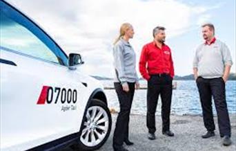 Taxi og tre personer som står foran sjøsanden