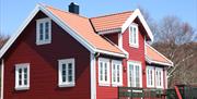 Lindesnes Camping og Hytteutleie - En stor rød hytte med hvite karmer, med grønn terrasse