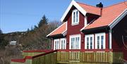 Lindesnes Camping og Hytteutleie - En stor rød hytte med hvite karmer, med grønn terrasse