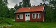 Grønt gress med rødt hus med hvit dør midt i, og to par vinduer med hvit ramme vedsiden av døra