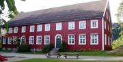 Høgtun Kultursenter, stort rødt bygning med hvite karmer. 20 vinduer på en vegg + 2 dører.