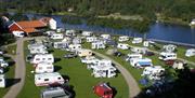 Bobil/Campingvogn på rekke og rad, med vei i mellom rekkene, Mandalselva like ved.