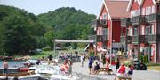 Mange mennesker på brygga ved den røde tregde feriehus på en solfylt dag