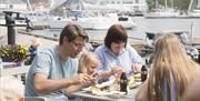 Familie på 4 som sitter ute og spiser god mat og drikker cola i glassflaske