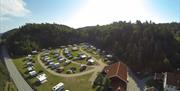Dronebilde av campingplassen med bobiler/Campingvogner på rekke og rad, med vei i mellom rekkene, hovedvei like ved og skog bak