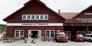 Lindesnes Hytteservice - Fasade. Brunrød bygning, med benker på utsiden
