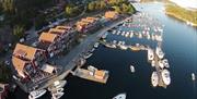 Bilde fra drone, brygge med mange båter og flere røde bygnjnegr langs brygga. På Tregde.