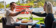 To personer med hvert sitt glass og skåler. Sitter ute i finværet, med en pizza på bordet