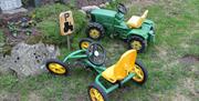 To grønne lekebiler, en traktor og en gocart lignende bil plassert ved lekeparkeingsplass.