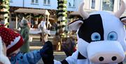 Et barn med nisselue hilser på en person utkledd i ku-maskotdrakt under julemarkedet i Lyngdal.