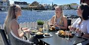 Tre jenter som smiler og spiser god mat hos Brygga