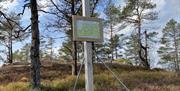 Bilde av stolpe med kart og to skilt. Retning til høyre: (rød bilde med figur som går) Bruskeland 4,0km. Retning til venstre: 3,5km Brukseland (blå bilde med figur som står på ski)
