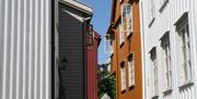 Det smale smuget på Øvre Tyholmen i Arendal med gamle hvite, rød og okerfargede trehus tett i tett med en smal brosteinsbelagt gate i mellom.