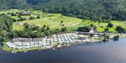 Oversiktsbilde av Solstrand Camping, mange campingvogner og hytter, er langs vannet, bak campingplassen er det store jorder og skog bak det igjen. blå himmel