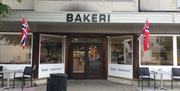 Inngangen med store bokstaver "BAKERI" over inngangsdøra. Norsk flagg hver side av inngange,