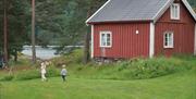 Red barn on green meadow with two kids on their way to the shore on Furøya.