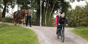 To smilende jenter sykler på en tandemsykkel, og en mann leier en brun hest med hvit bliss bak jentene.