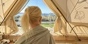 Jente med rufsete hestehale tullet inn i teppet inni glampingteltet og ser ut mot landskapet