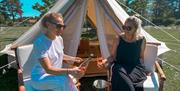 to damer sittende foran glampingtelt som drikker noe kjølende i sola