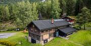 flyfoto av Hillestad galleri, en tømmerbygning omgitt av grønt gress og skog.
