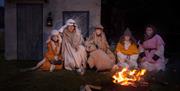 Skuespillere utkledd som gjetere sitter samlet rundt et bål foran en enkel stallvegg under forestillingen «Veien til Betlehem» i Lyngdal.