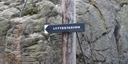 Svart skilt med hvit skrift "Lyttestasjon" på en stolpe