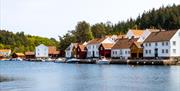 Flere hus langs vannet og båter langs bryggen ved Furuholmen