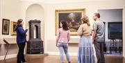 Fire personer inne på museet ser på det store maleriet «Haugianerne» på Mandal museum, der Adolph Tidemand skildrer lekpredikanten Hans Nielsen Hauges følgere.