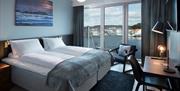 Hotellrom, dobbeltseng med Tv og pult. En godstol ved vinduet, der utsikten er ut mot vannet og sentrum