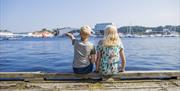 To barn som sitter med ryggen til på brygga i Mandal med utsikt ut over elva