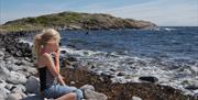 jente sitter på rullesteinsstrand på sørsiden av Merdø utenfor Arendal