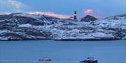 Vakker kveld ut mot fyret, to båter på vannet og snø på holmen, med fyret ca midt på bilde. skyene er rosa