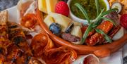 Matbilde tapastallerken, små pizzastykker, peperoni og skinke rullet sammen, liten skål med diverse snacks oppi. Blåbær, bringebær, physalis , ost, og en grønn dipp i midten.