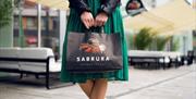 Person i grønn kjole som holder en papirpose med Sabrura logoen