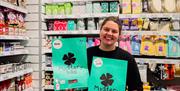 Smilende ansatt fra Normal, viser frem "Mystery Bag" foran hylle med varer