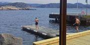 Utsikt gjennom vinduet på badstua, ut mot havet og to personer som går på brygga på vei for å bade