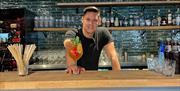 bartender bak bardisken som holder frem en fristende drink