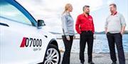 Taxi og tre personer som står foran sjøsanden