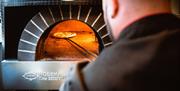 pizzabaker steker pizza på lang fjøl i ovnen